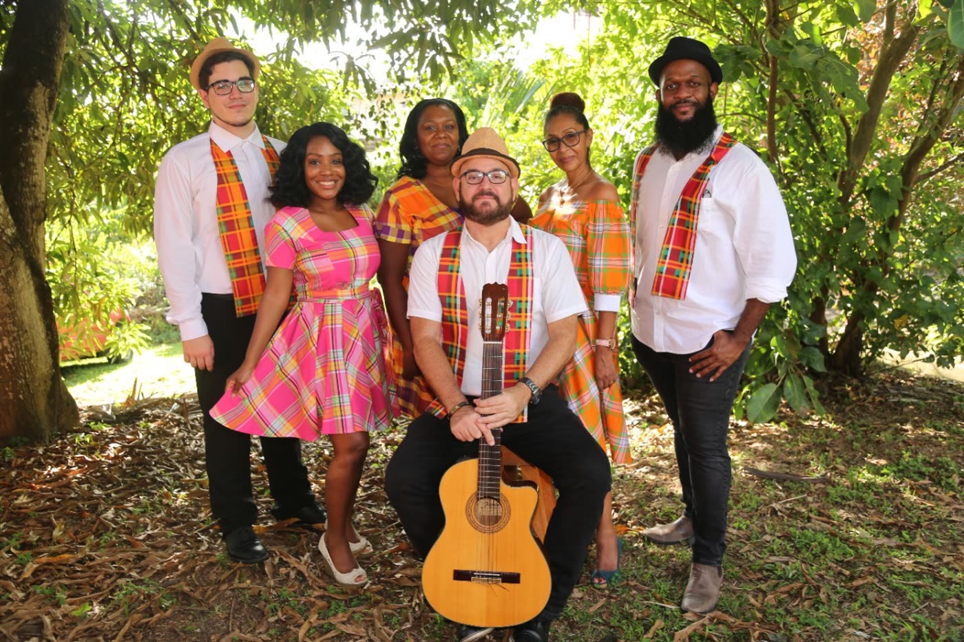 The Tout Bagay Patwa choir in bright Madras-plaid attire, gathered under a tree with a guitar